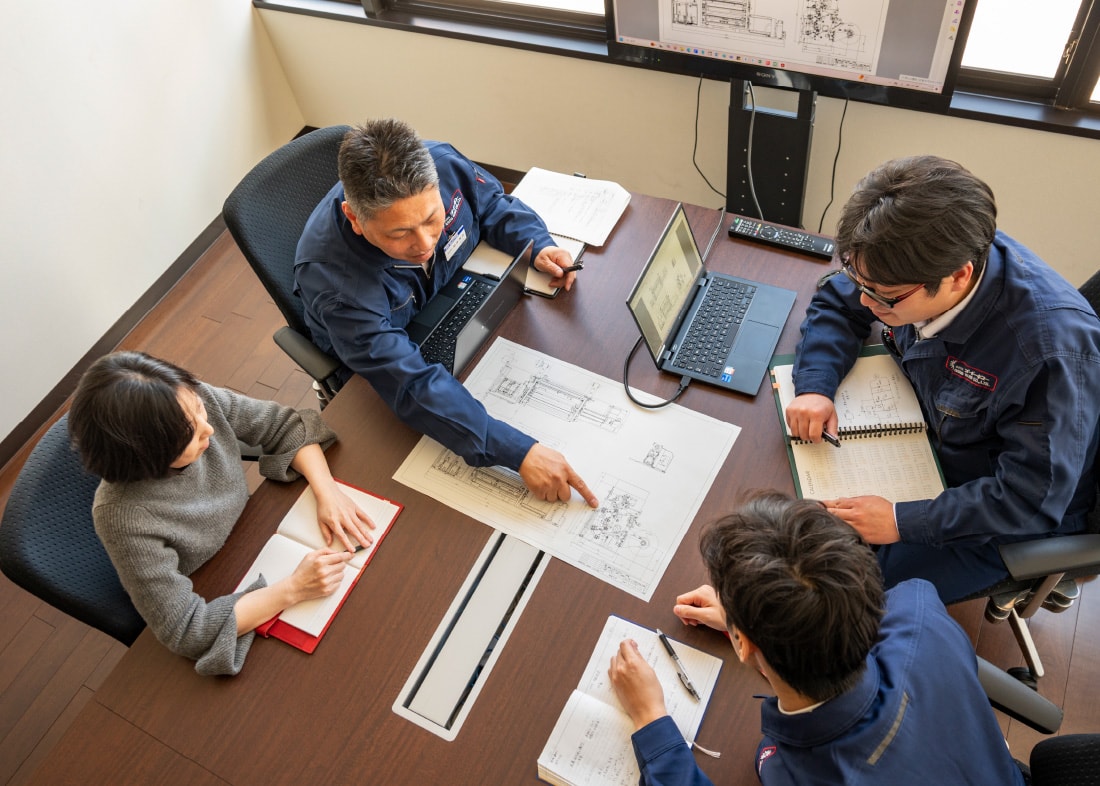 Employees discussing around a table with spread blueprints