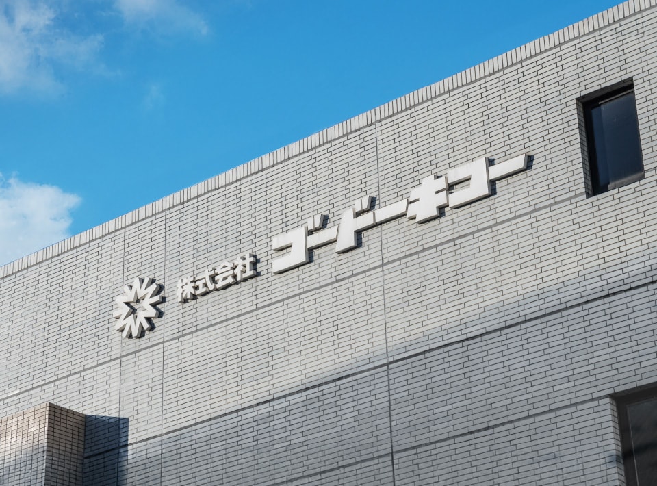 青空を背景に社名ロゴを掲げた自社ビルの外観