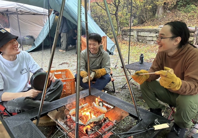 焚き火を囲んでキャンプ料理を楽しむ3人