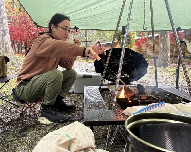 テント脇の焚き火で料理をする社員